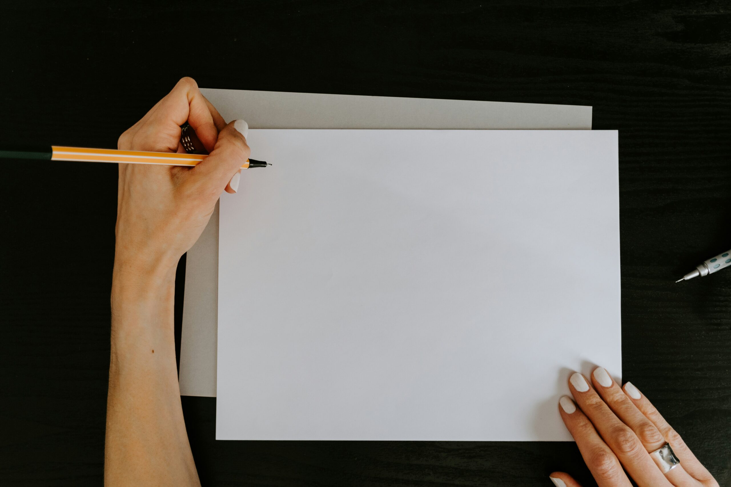 aerial view of woman holding pen to the top of a blank sheet of paper